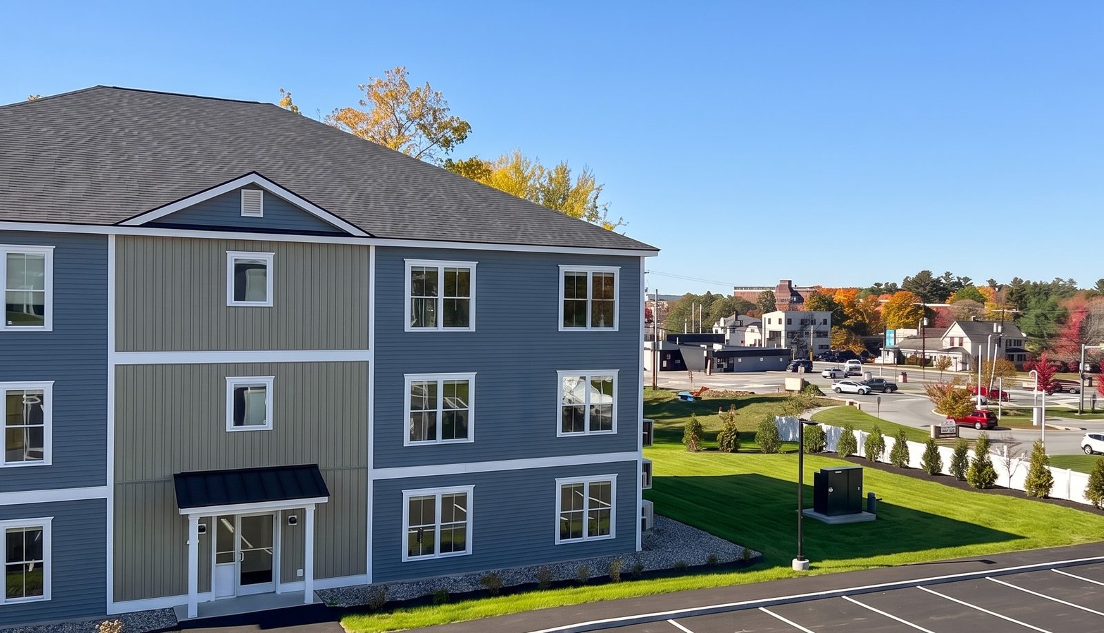 A corner view of the GALE building in autumn: blue and sage siding, white trim, a covered entry, and a lawn with young evergreens beside the parking area
