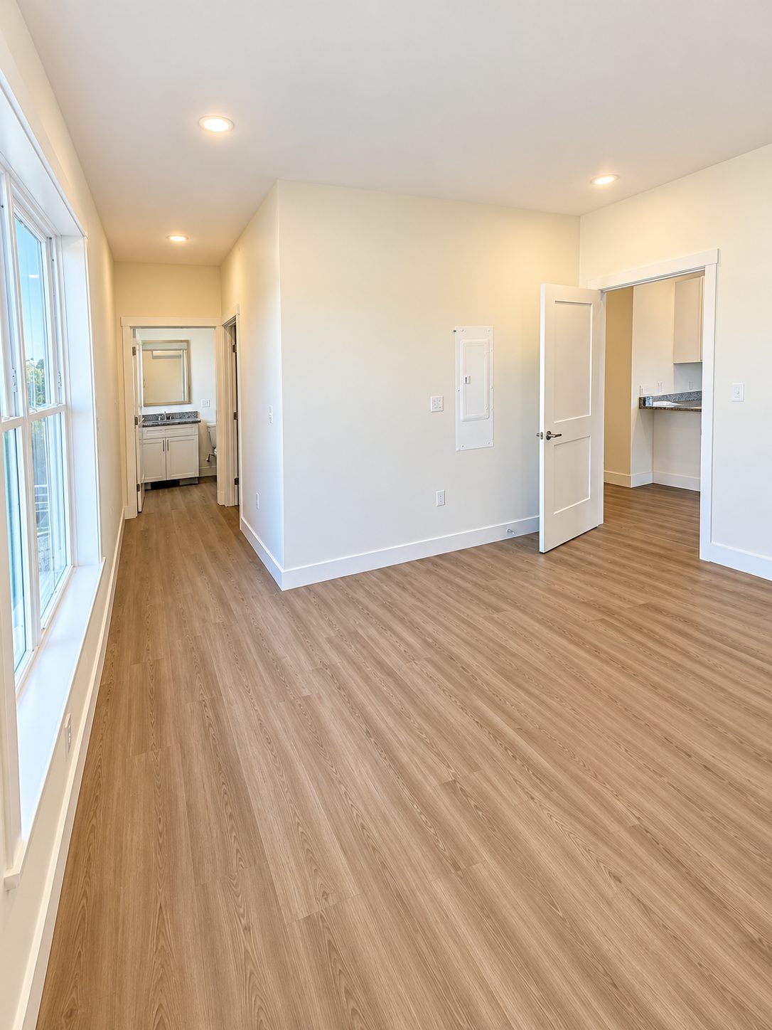 Looking out from a bedroom in a GALE residence, past a tall window, toward the bathroom doorway and the kitchen beyond