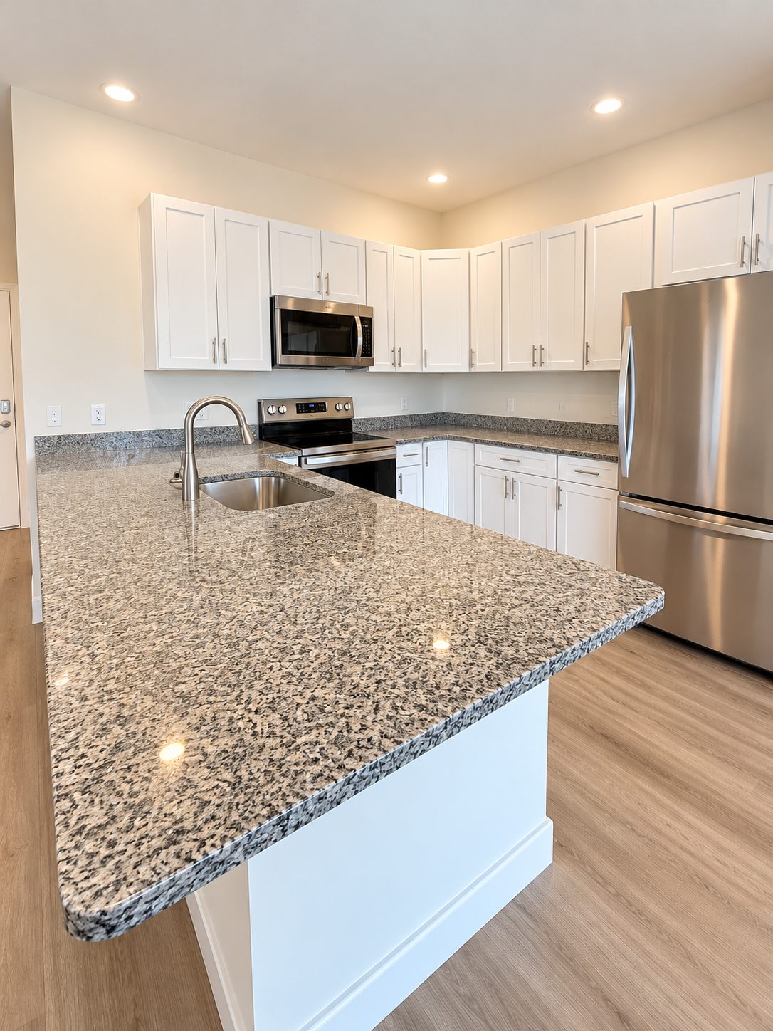 A GALE kitchen with a granite peninsula and undermount sink, white shaker cabinets, a stainless steel range, microwave, and refrigerator, and wood-look plank floors